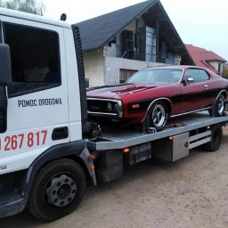 LAWETA Pomoc Drogowa TUCHÓW Transport HOLOWANIE - Biała ciężarówka pomocy drogowej z napisem 'POMOC DROGOWA' i numerem telefonu przewozi na platformie czerwony, klasyczny samochód osobowy Dodge Charger z czarnym pasem wzdłuż boku.