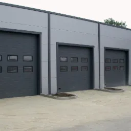 Szereg szarych segmentowych drzwi z oknami w hali przemysłowej, jedna brama lekko otwarta, widoczny betonowy podjazd.