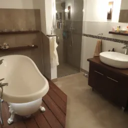 Nowoczesna łazienka z wolnostojącą wanną na drewnianym podeście, kabiną prysznicową ze szklanymi drzwiami i umywalką nablatową na ciemnej szafce.