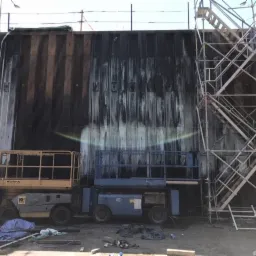 Czyszczenie metalowej ściany za pomocą myjki ciśnieniowej z podnośnika koszowego i rusztowania, widoczne ślady po czyszczeniu.