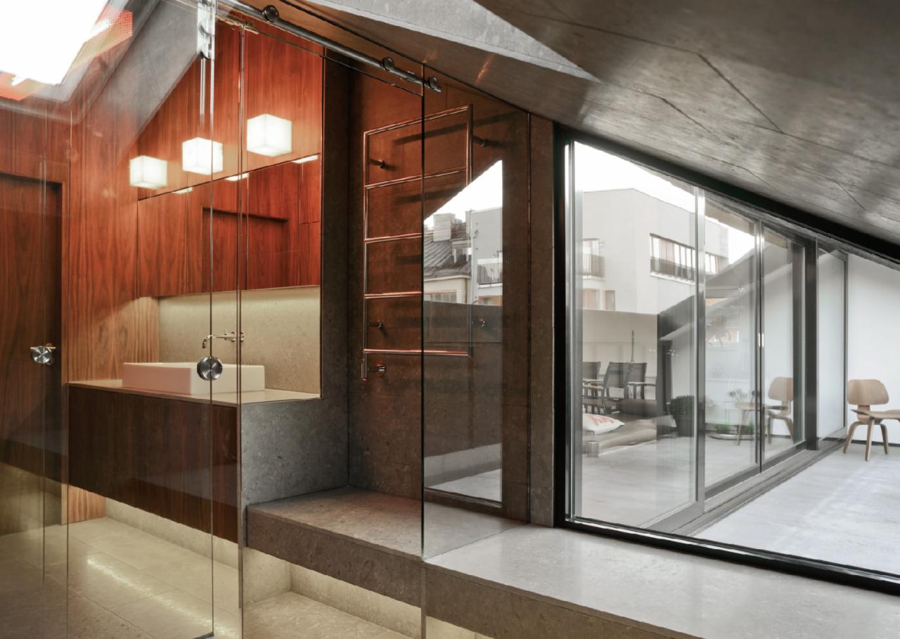 Nowoczesna łazienka na poddaszu z drewnianymi szafkami, kamienną umywalką i widokiem na taras przez przesuwne szklane drzwi.