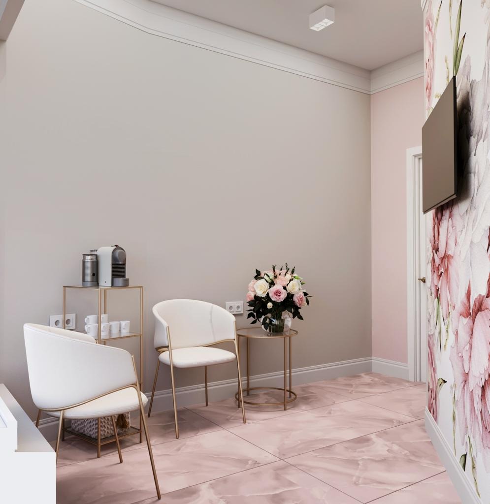Eleganckie wnętrze poczekalni: białe krzesła na złotych nogach, stolik z kwiatami, ekspres do kawy i ściana z motywem kwiatowym. Marmurowa podłoga w odcieniach różu.
