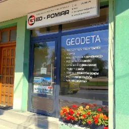 Fasada biura geodezyjnego z szyldem GEO-POMIAR, widoczne usługi: mapa do celów projektowych, tyczenie, podział nieruchomości, projekty domów i projektowanie zjazdów.