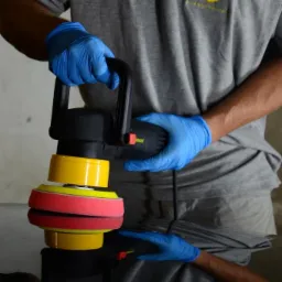 Polerowanie lakieru samochodu polerką elektryczną z żółto-czerwonym padem, widoczne odbicie w lakierowanej powierzchni.