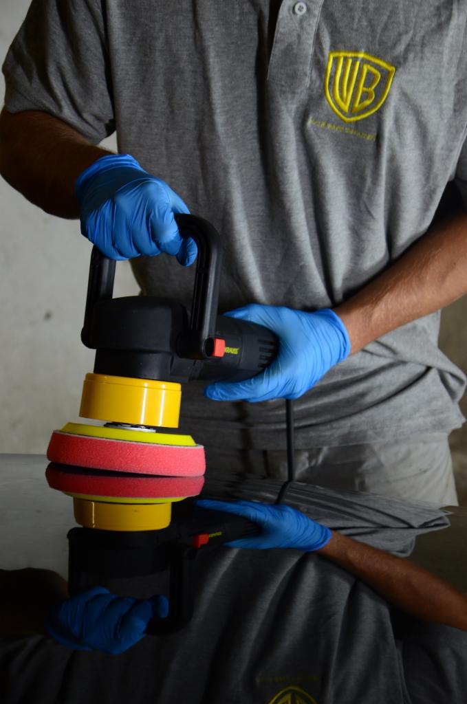 Polerowanie lakieru samochodu polerką elektryczną z żółto-czerwonym padem, widoczne odbicie w lakierowanej powierzchni.