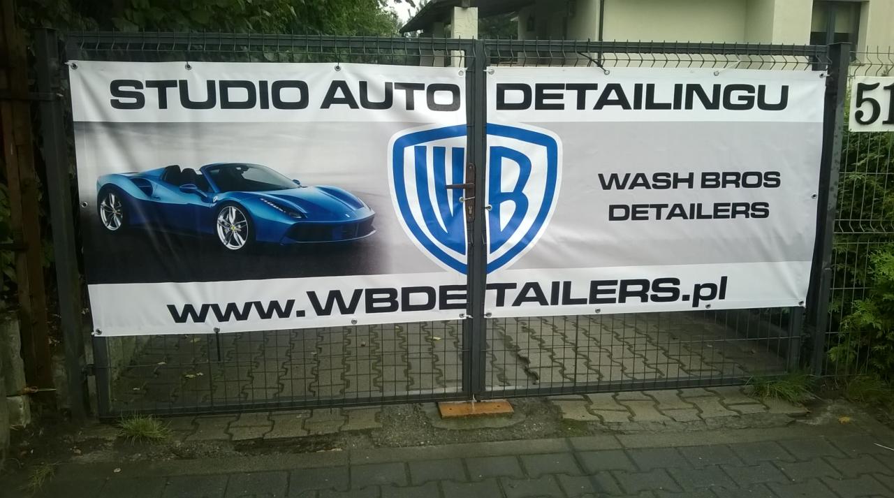 Baner reklamowy 'Studio Auto Detailingu' z logo 'Wash Bros Detailers', prezentujący zdjęcie niebieskiego sportowego kabrioletu, umieszczony na metalowej bramie.
