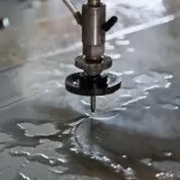 Proces cięcia metalu strumieniem wody pod ciśnieniem. Widoczne dysza, metalowy arkusz i woda z oparami.