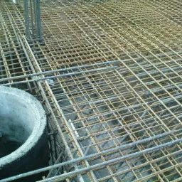 Siatka zbrojeniowa przygotowana do zalania betonem, z widocznym betonowym kręgiem studziennym w lewym dolnym rogu.