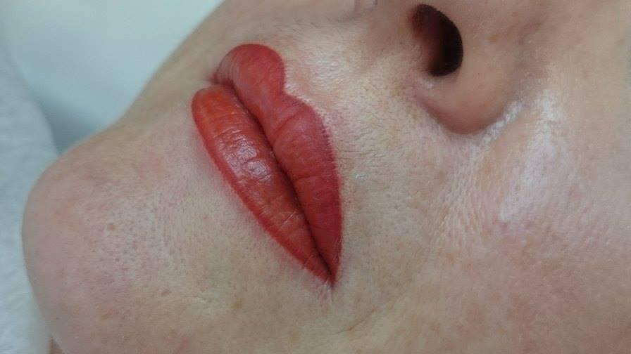 Zbliżenie na usta po zabiegu makijażu permanentnego w odcieniu intensywnej czerwieni, widoczne zaczerwienienie skóry wokół ust.