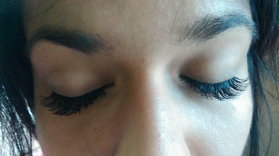 Zbliżenie na zamknięte oczy kobiety z przedłużonymi, gęstymi, czarnymi rzęsami, widoczne naturalne brwi.