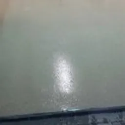 Jasna, połyskliwa posadzka przemysłowa w hali, widoczne ślady po wałku, szara listwa przypodłogowa, w tle regał z narzędziami i akcesoriami.