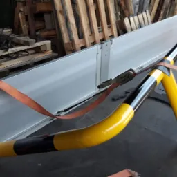 Transport zabezpieczonej metalowej konstrukcji z Goli przy użyciu pasów transportowych i żółto-czarnej bariery ochronnej.