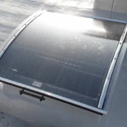 Zamontowane na dachu świetlik z poliwęglanu z ramą z profili aluminiowych, zabezpieczony stalowymi linkami.