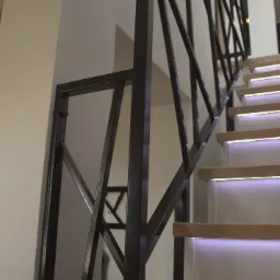 Nowoczesna, ciemna balustrada metalowa o geometrycznym wzorze na schodach z podświetleniem LED.