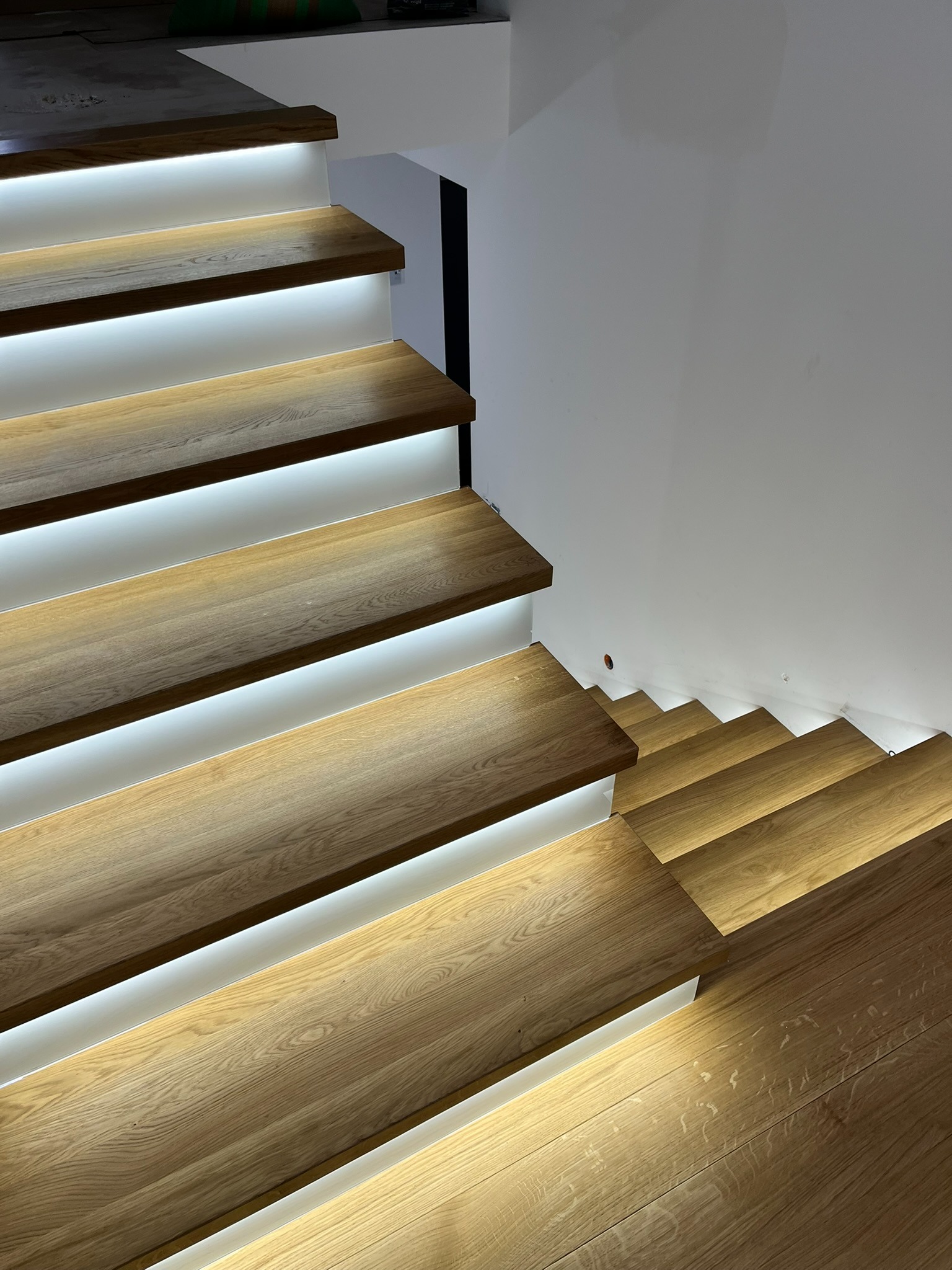 Nowoczesne schody z drewna dębowego z subtelnym podświetleniem LED, tworzące ciepłą atmosferę. Ujęcie z góry podkreśla minimalistyczny design i precyzję wykonania.