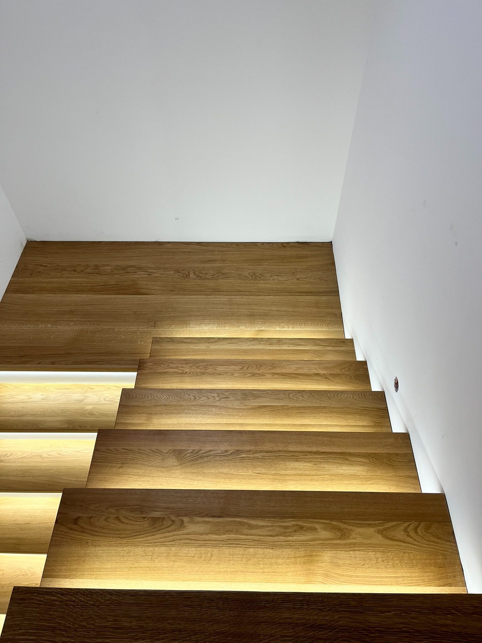 Nowoczesne schody z drewna z subtelnym podświetleniem LED, widok z dołu. Minimalistyczne wykończenie, ciepłe światło podkreśla naturalny rysunek drewna.