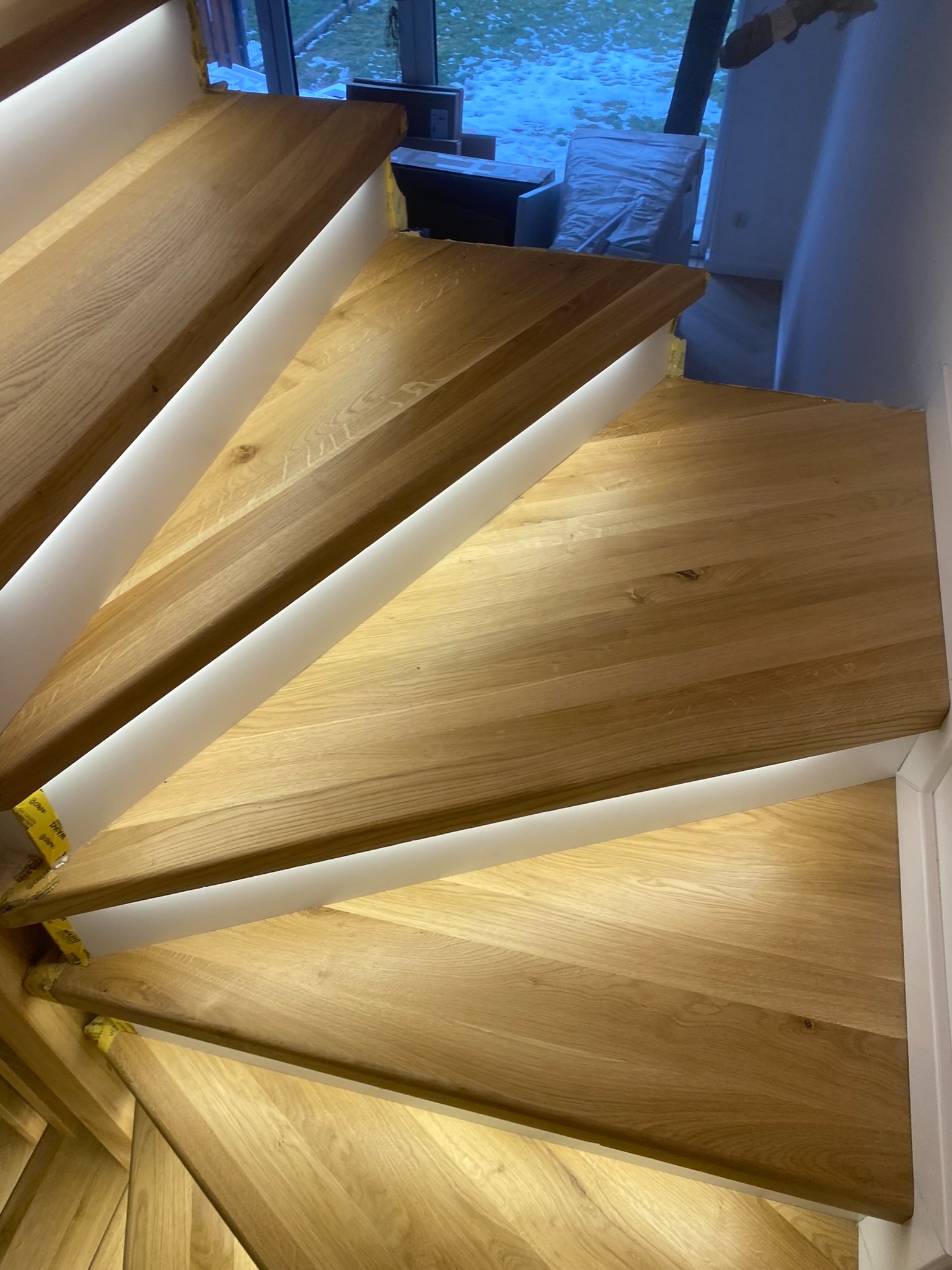 Bieg drewnianych schodów z podświetleniem LED, widok z góry, ukazujący naturalny rysunek drewna i precyzyjne wykonanie, z elementami wykończenia w bieli.