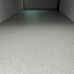 Jasnoszara posadzka z drobnymi czarnymi i białymi inkluzjami, świeżo wylana w pomieszczeniu z szarymi ścianami i oknem zabezpieczonym folią.