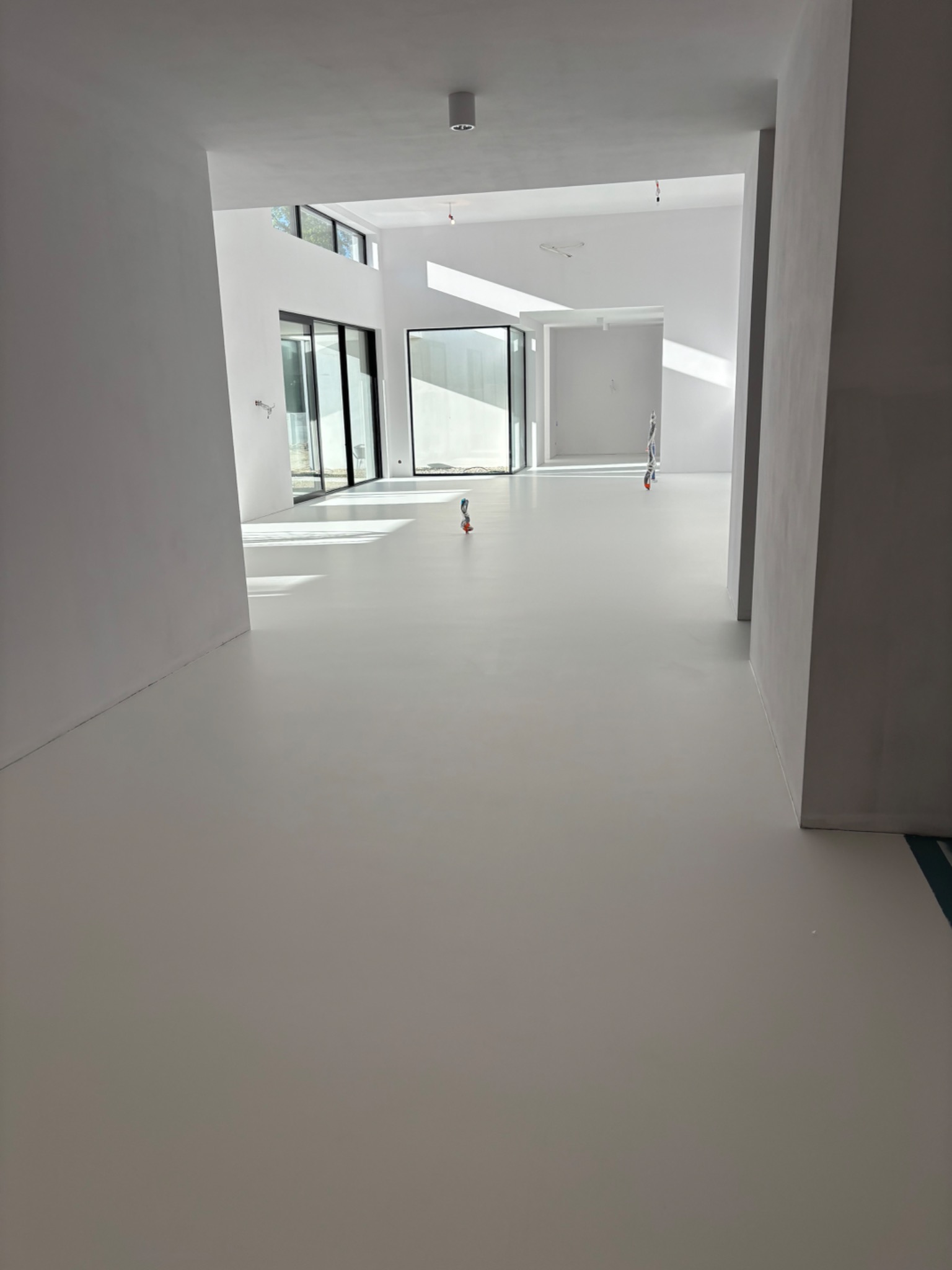 Jasnoszara, gładka podłoga w przestronnym, minimalistycznym wnętrzu z dużymi oknami, widoczne kable wystające z podłogi, sugerujące prace wykończeniowe.