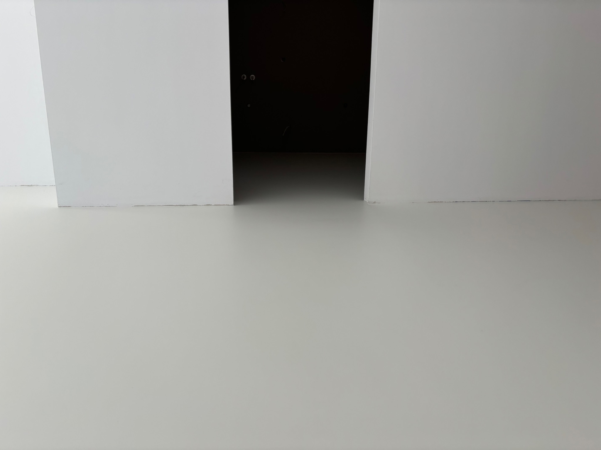 Jasnoszara, gładka podłoga w Woli Rzędzińskiej, widoczna pomiędzy białymi ścianami i ciemnym przejściem do innego pomieszczenia.