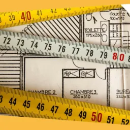 Plan architektoniczny domu z wymiarami pomieszczeń, częściowo zasłonięty przez trzy rozłożone miarki zwijane w kolorach żółtym i białym, logo firmy MM|DOM w prawym górnym rogu.