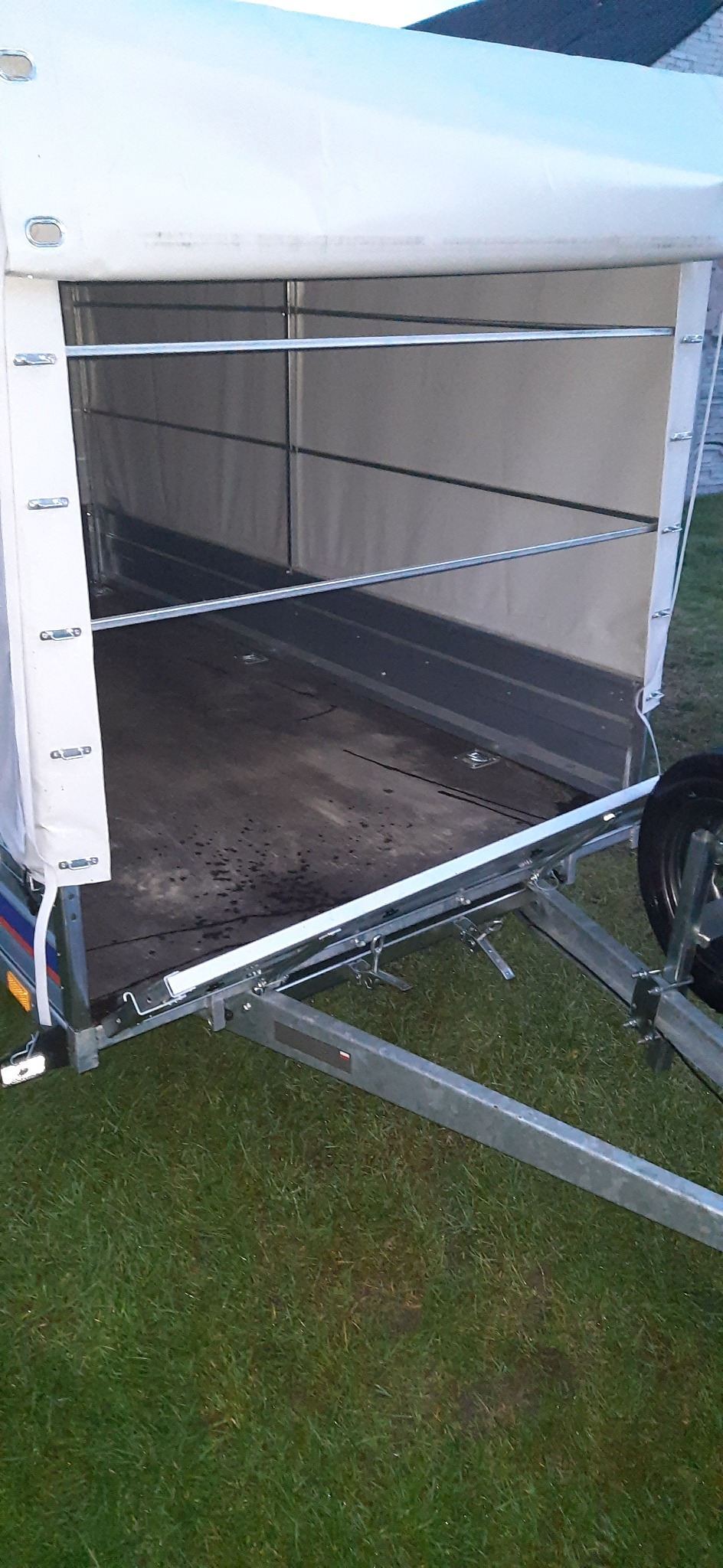 Otwarta przyczepa z plandeką, widoczna pusta przestrzeń ładunkowa i metalowe zabezpieczenia boczne.