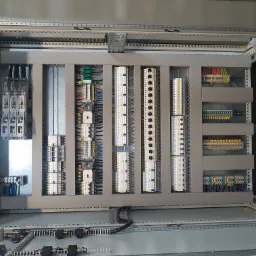 Wnętrze szafy sterowniczej z widocznymi modułami, przewodami i listwami zaciskowymi, ułożonymi w uporządkowany sposób.