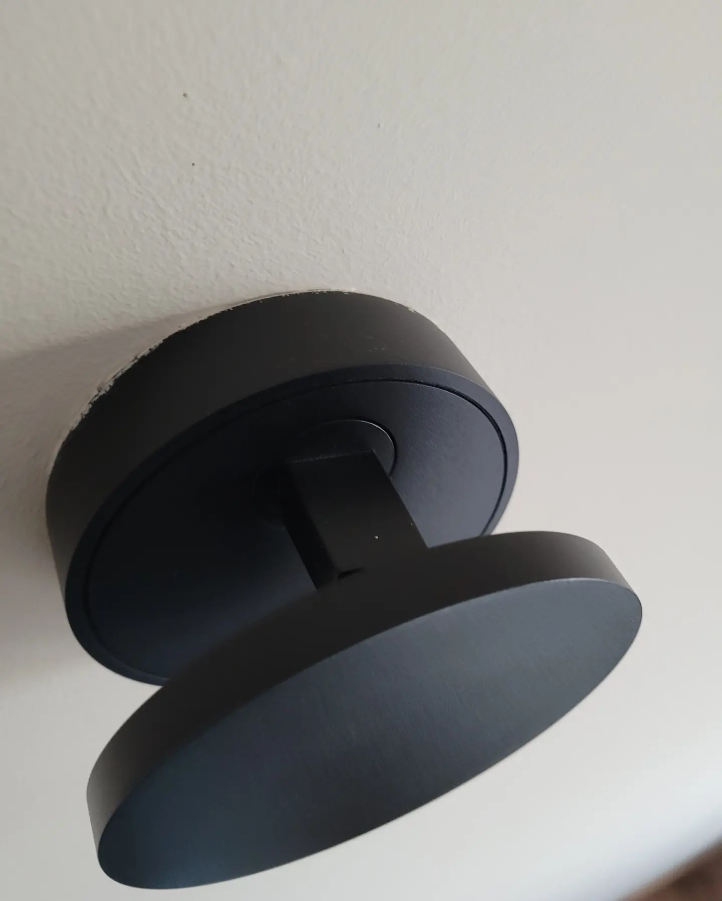 Czarna, okrągła lampa sufitowa z regulowanym kątem świecenia, zamontowana na białym suficie. Widoczne ślady po montażu.