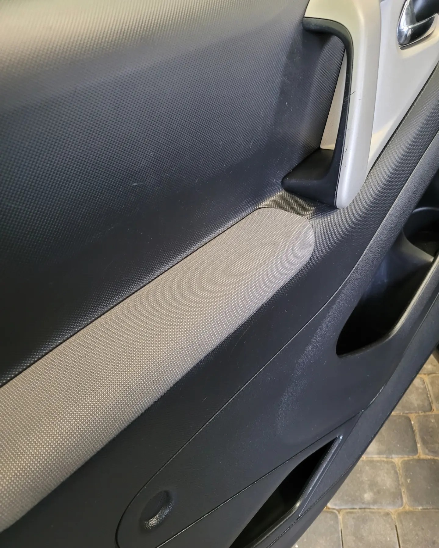 Wnętrze samochodu: czarno-szare obicie drzwi z teksturowanym panelem i srebrną klamką, ukazujące detale materiałów i ergonomiczny design.