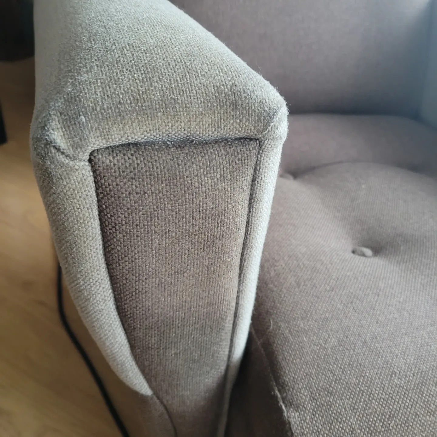 Szczegółowe ujęcie brązowego fotela tapicerowanego z widoczną fakturą materiału i guzikiem na siedzisku, ukazujące potencjalne zabrudzenia na podłokietniku.