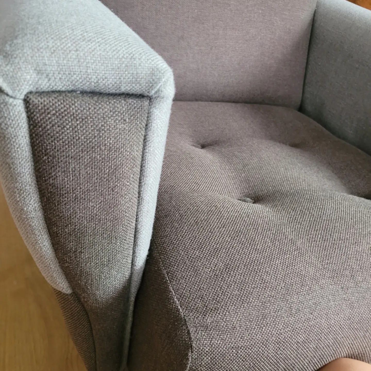 Szczegółowe ujęcie szarego fotela tapicerowanego z guzikami, prezentujące fakturę materiału i solidne wykonanie. Widoczny fragment podłogi.