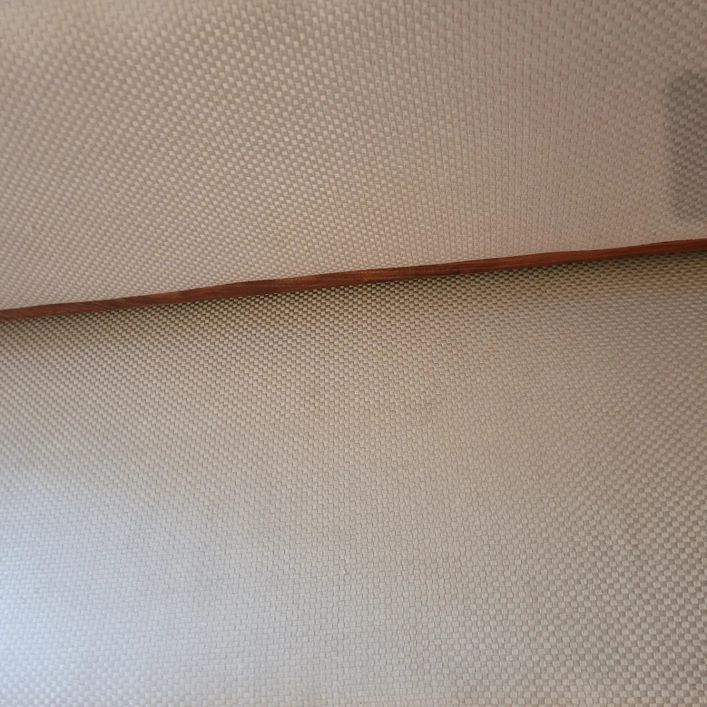 Delikatna, beżowa tapicerka z drobnym wzorem, oddzielona drewnianą listwą. Widok z bliska, ukazujący strukturę materiału i subtelny odcień.