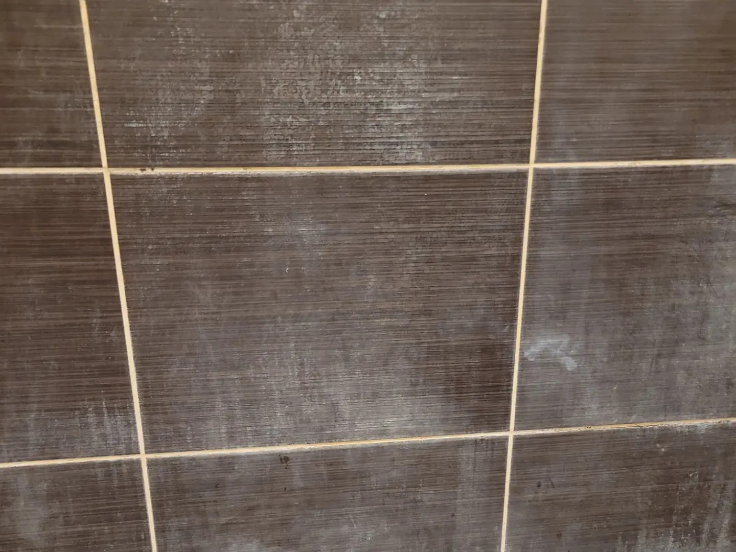 Brudne, brązowe płytki ceramiczne z jasnymi fugami, widoczne zacieki i osad, wymagające czyszczenia. Powierzchnia matowa, oświetlenie naturalne.