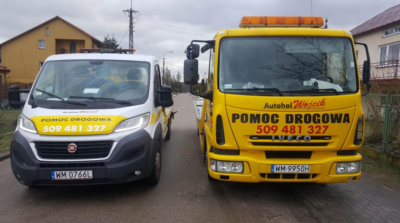 Dwa pojazdy pomocy drogowej w Mrozach: biały Fiat Ducato i żółty Iveco, oba z widocznym numerem telefonu kontaktowego i napisem 'Pomoc Drogowa'.