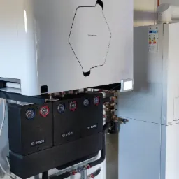 Nowoczesny system wentylacyjny z rekuperacją Thessla Green, z trzema czarnymi modułami Bosch, widoczne rury wentylacyjne i instalacja na szarej podłodze z płytek.