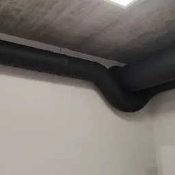 Czarne, zaizolowane rury wentylacyjne pod betonowym sufitem w pomieszczeniu. Widoczne łączenia rur.