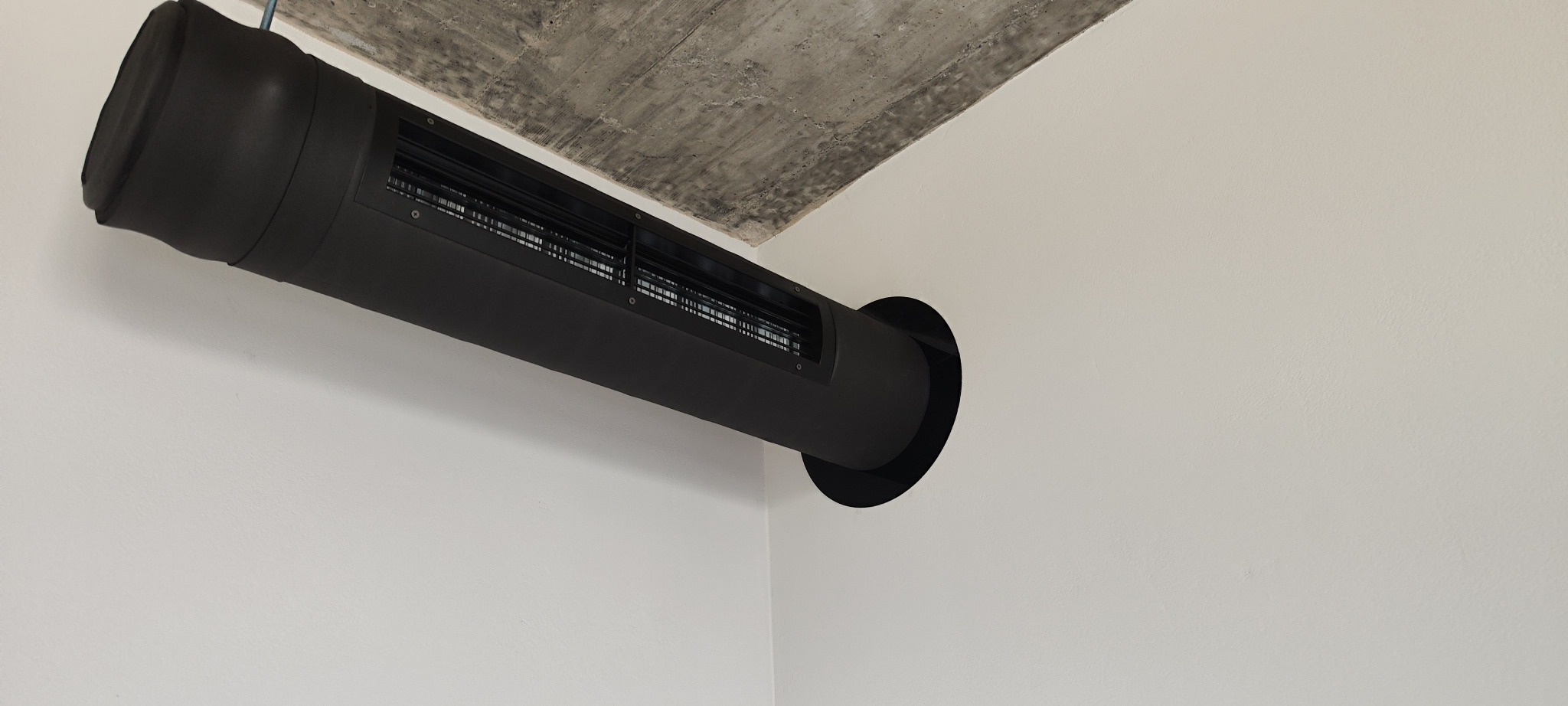 Czarny kanał wentylacyjny zamontowany w rogu pomieszczenia w Bielsko-Białej. Widoczna kratka wentylacyjna i betonowy sufit.