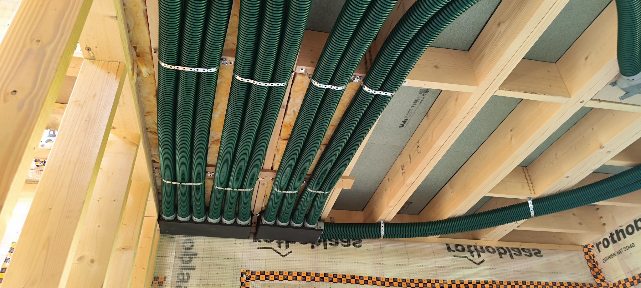 Zielone rury wentylacyjne zamocowane do drewnianej konstrukcji stropu, widok z dołu. Izolacja widoczna między rurami. Nowoczesna instalacja wentylacyjna.