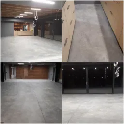 Szara, gładka podłoga w dużym pomieszczeniu z widocznymi instalacjami elektrycznymi zwisającymi z sufitu oraz fragmentami zabudowy kuchennej i ścian z cegły klinkierowej.