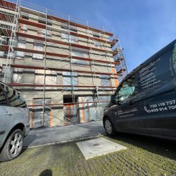 Termodocieplenia.pl - Budynek wielorodzinny w trakcie prac elewacyjnych, rusztowania pokrywają fasadę, okna zabezpieczone folią, obok zaparkowany samochód osobowy i firmowy bus z reklamą usług termoizolacyjnych.
