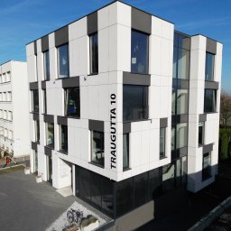 Termodocieplenia.pl - Nowoczesny budynek biurowy z elewacją w biało-szare pasy, z dużymi oknami, widziany z góry w słoneczny dzień. Na elewacji widoczny adres: Traugutta 10.