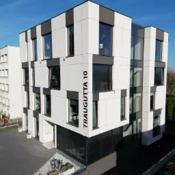 Nowoczesny budynek biurowy z elewacją w biało-szare pasy, z dużymi oknami, widziany z góry w słoneczny dzień. Na elewacji widoczny adres: Traugutta 10.