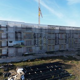 Termodocieplenia.pl - Wielopiętrowy budynek w trakcie ocieplania elewacji, osłonięty siatką z reklamami, widoczny dźwig budowlany i materiały budowlane na ziemi.