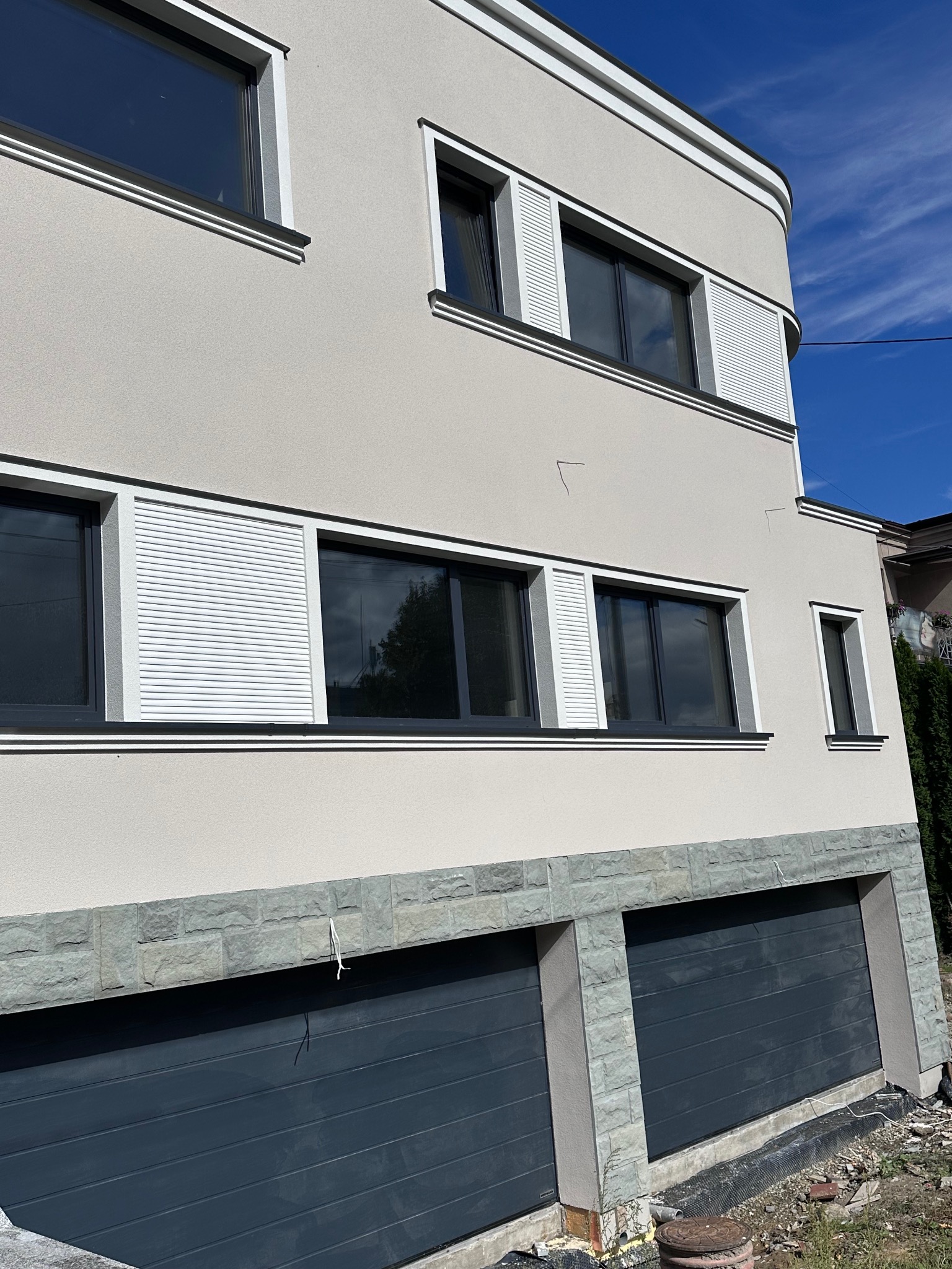 Dwupiętrowy dom z jasną elewacją, szarymi ramami okiennymi i białymi żaluzjami, widok z dołu na narożnik budynku i niebieskie niebo