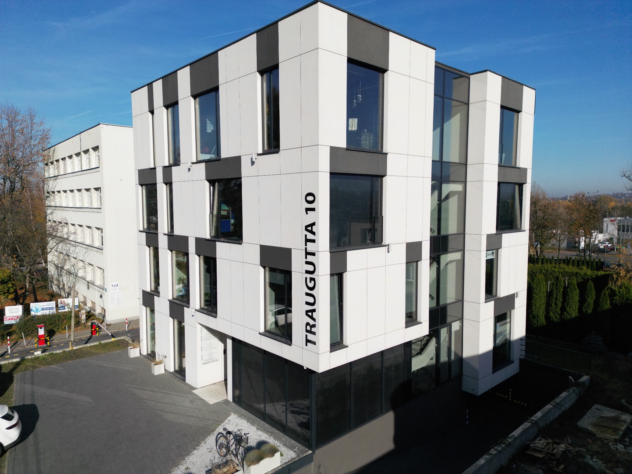 Nowoczesny budynek biurowy z elewacją w biało-szare pasy, z dużymi oknami, widziany z góry w słoneczny dzień. Na elewacji widoczny adres: Traugutta 10.