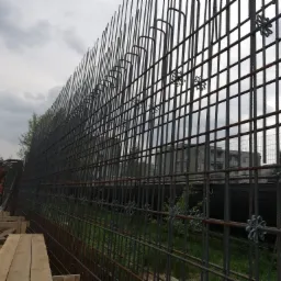 Konstrukcja zbrojeniowa pionowej ściany, widoczne dystanse w kształcie gwiazdek, szare niebo w tle.