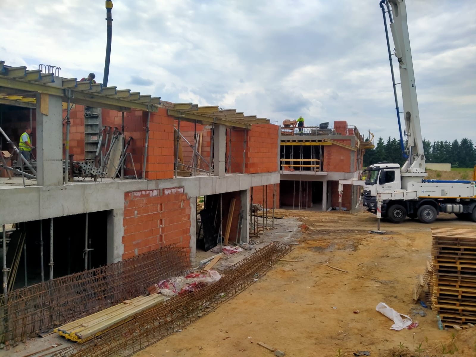 Budowa dwóch domów w stanie surowym otwartym, widoczny betonowy szkielet, czerwona cegła, stalowe zbrojenia i dźwig do betonu.