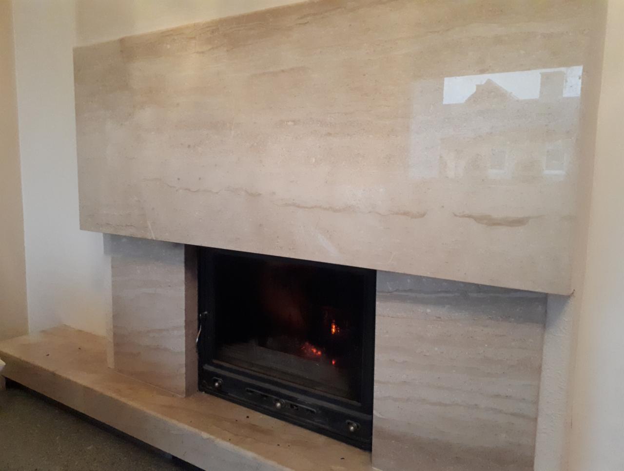 Obudowa kominka z trawertynu z widocznym odbiciem budynku w polerowanej powierzchni.