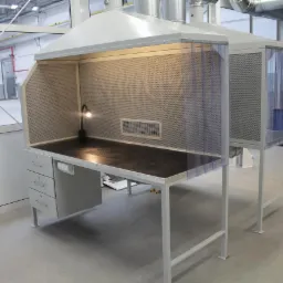 Dwa stanowiska robocze z odciągiem miejscowym i oświetleniem punktowym, w hali produkcyjnej z widocznymi instalacjami wentylacyjnymi pod sufitem.