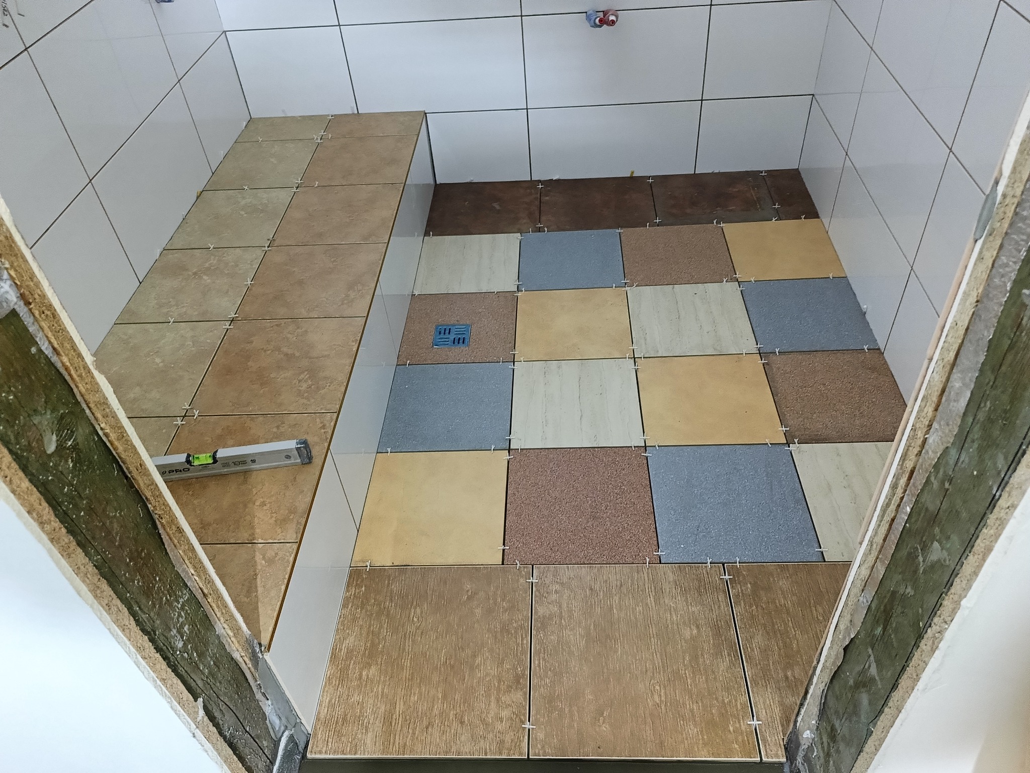 Układanie płytek podłogowych w kabinie prysznicowej z użyciem krzyżyków dystansowych i poziomicy przy progu.